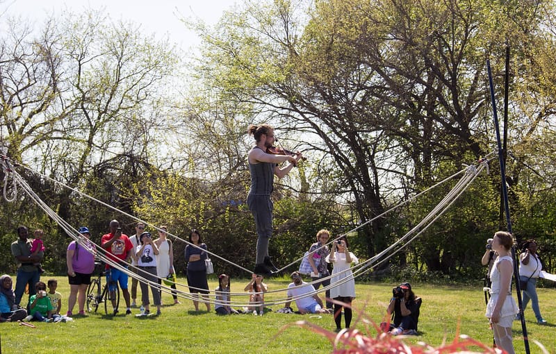 A man is on a rope in the air playing an instrument while people watch and take photos.
