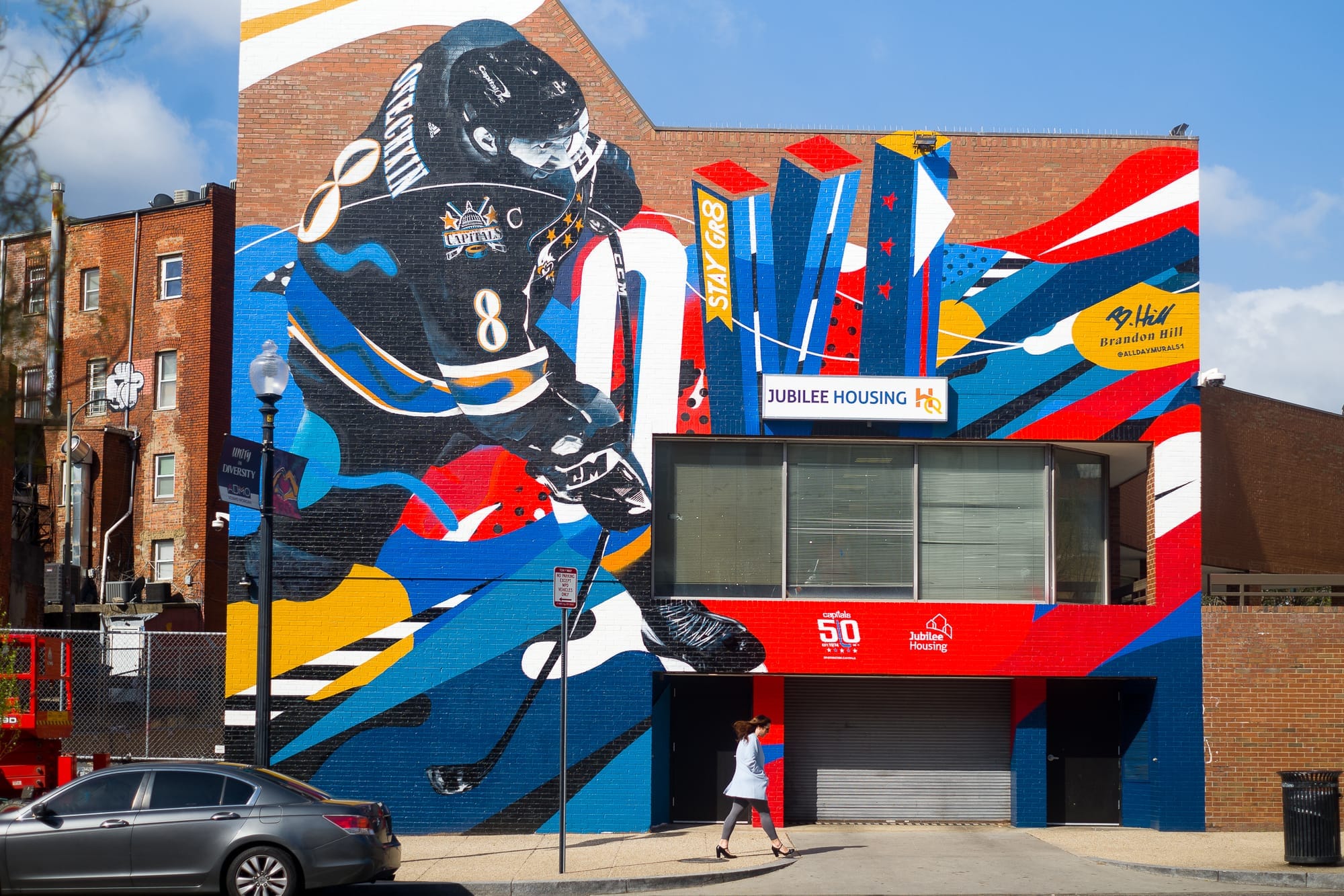 A black, white, red, yellow, and blue mural on a red brick wall depicts Washington Capitals player Alexander Ovechkin.