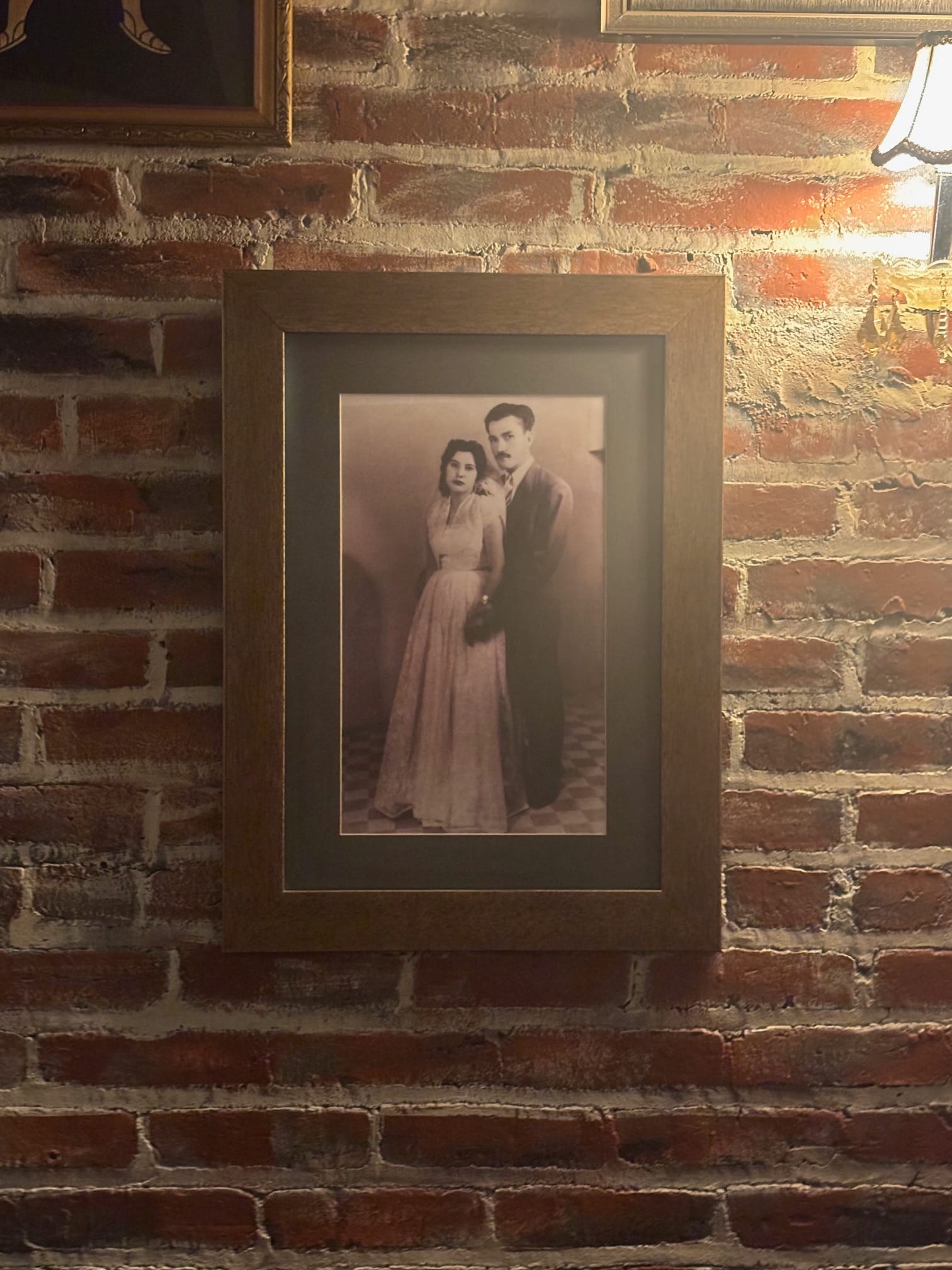 A black and white photograph of the restaurant owner's parents framed and hung on a brick wall.