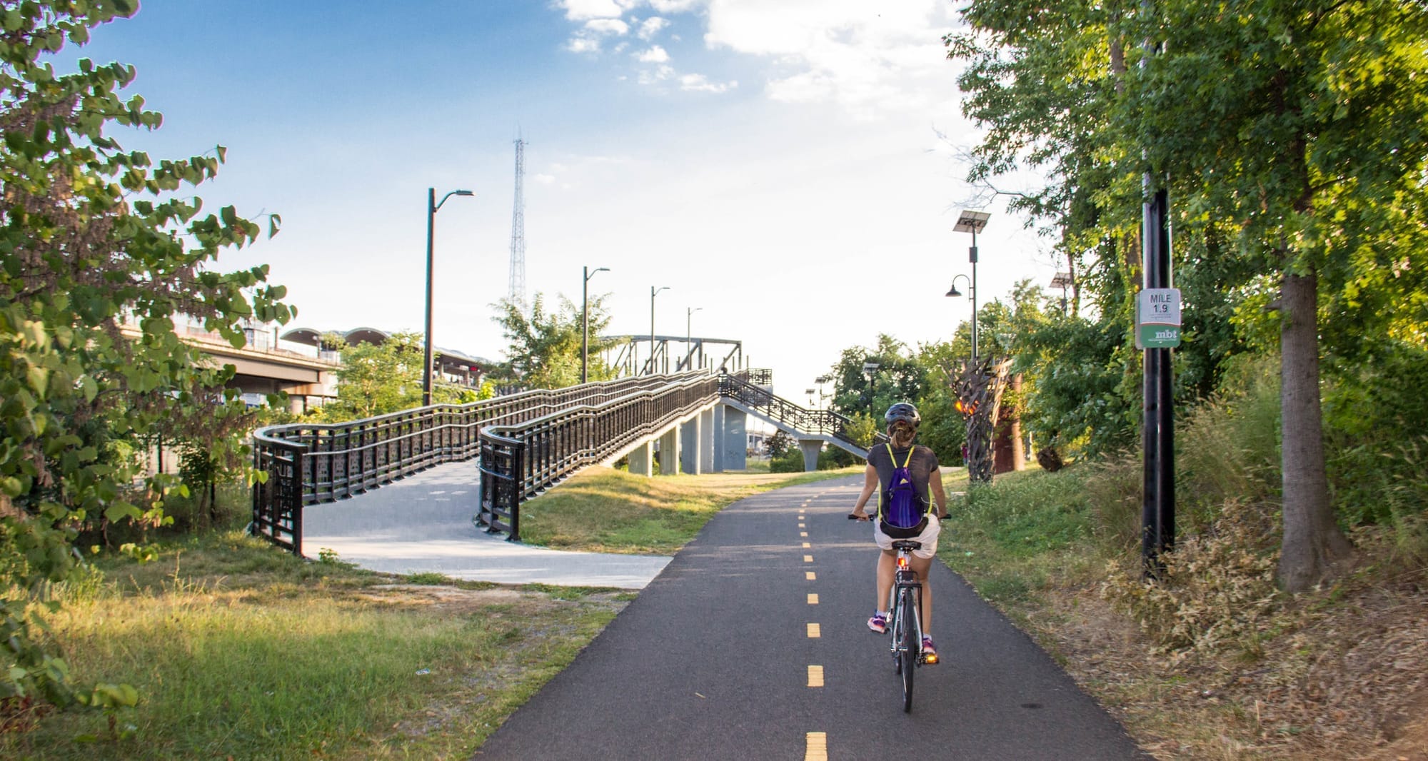 A person rides a bike along a paved path, with a bridge extending out to the left. 