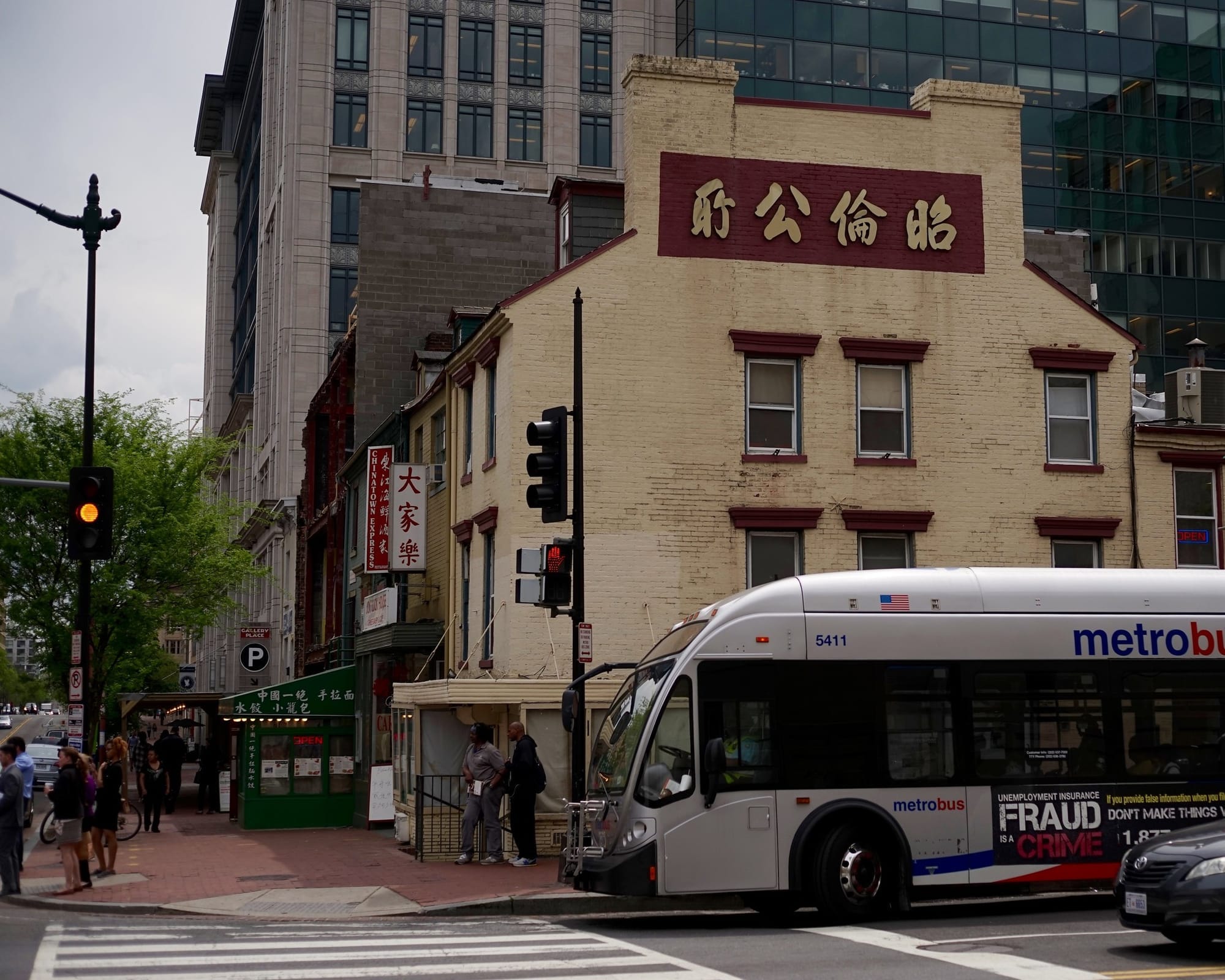 A view of an intersection in D.C.'s Chinatown, with a yellow light and a red walk signal. A metrobus is visible in the frame, and businesses with Chinese lettering are visible in the backgrou