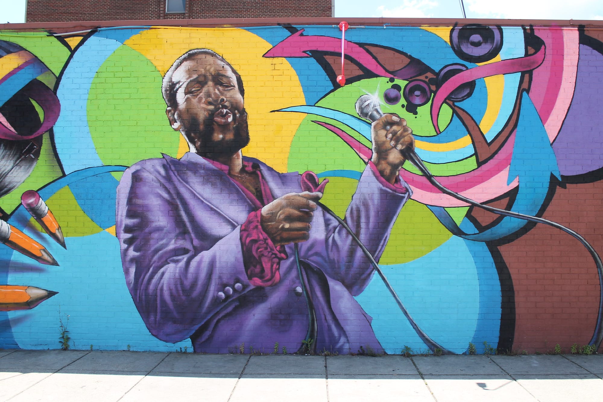 A mural of a Black man in a purple suit holding a microphone mid-sing. 