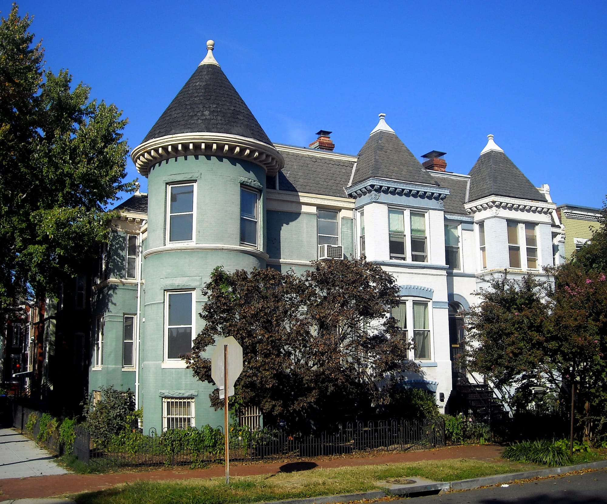 Green, white, and violet rowhouses with turrets and trees in the front in Capitol Hill.