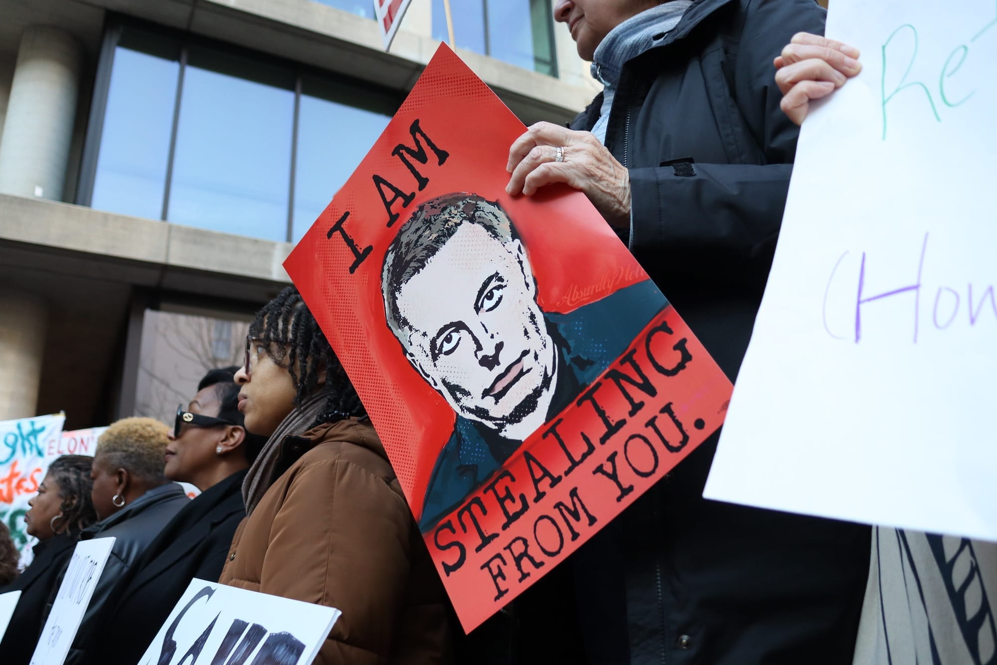 A protestor holds a poster with a picture of Elon Musk that reads: "I am stealing from you."