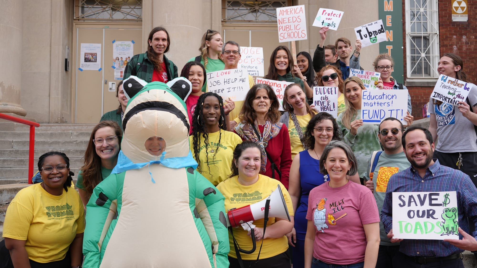 Teachers hold signs and pose for a photo on the stairs in front of Tubman Elementary.