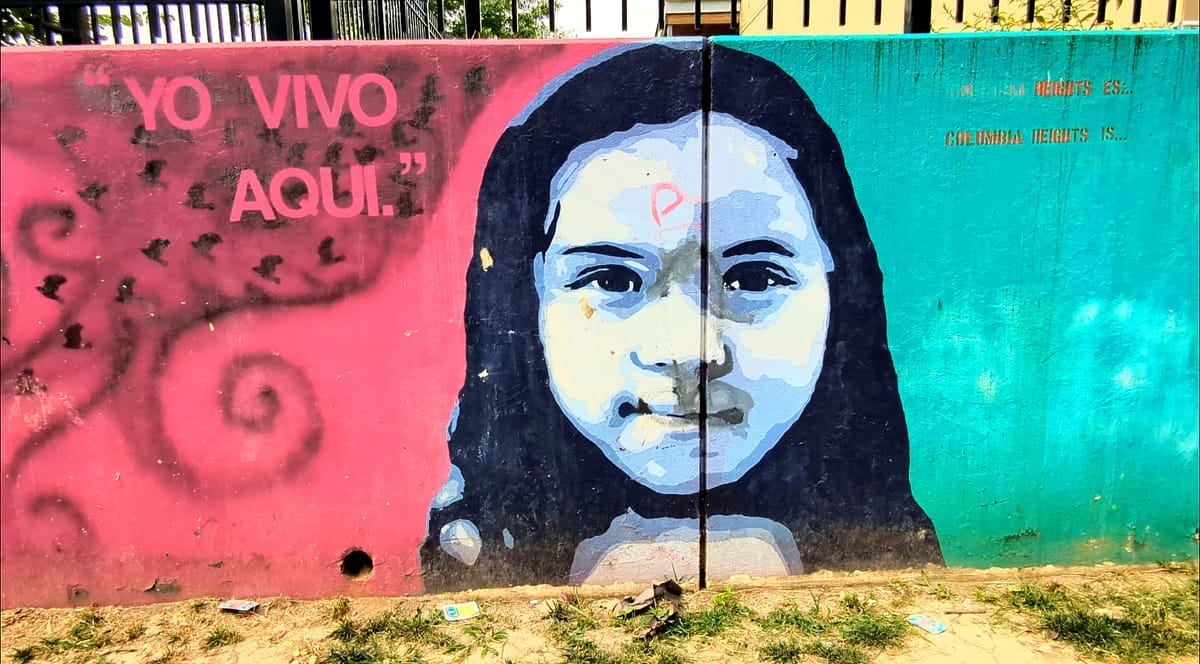 Mural of young girl with Yo Vivo Aqui written to her left in red and green painted on her right.
