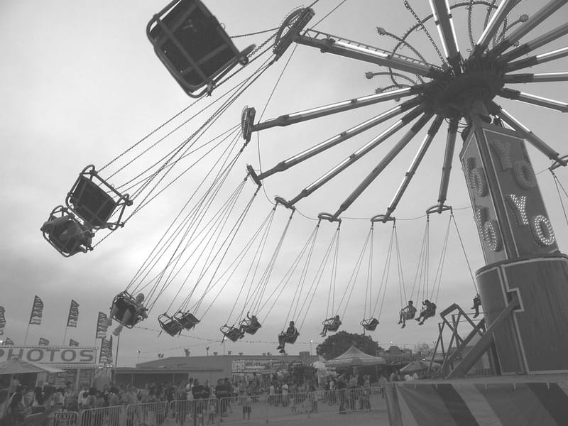 Black and white photo of swinging ride at carnival.