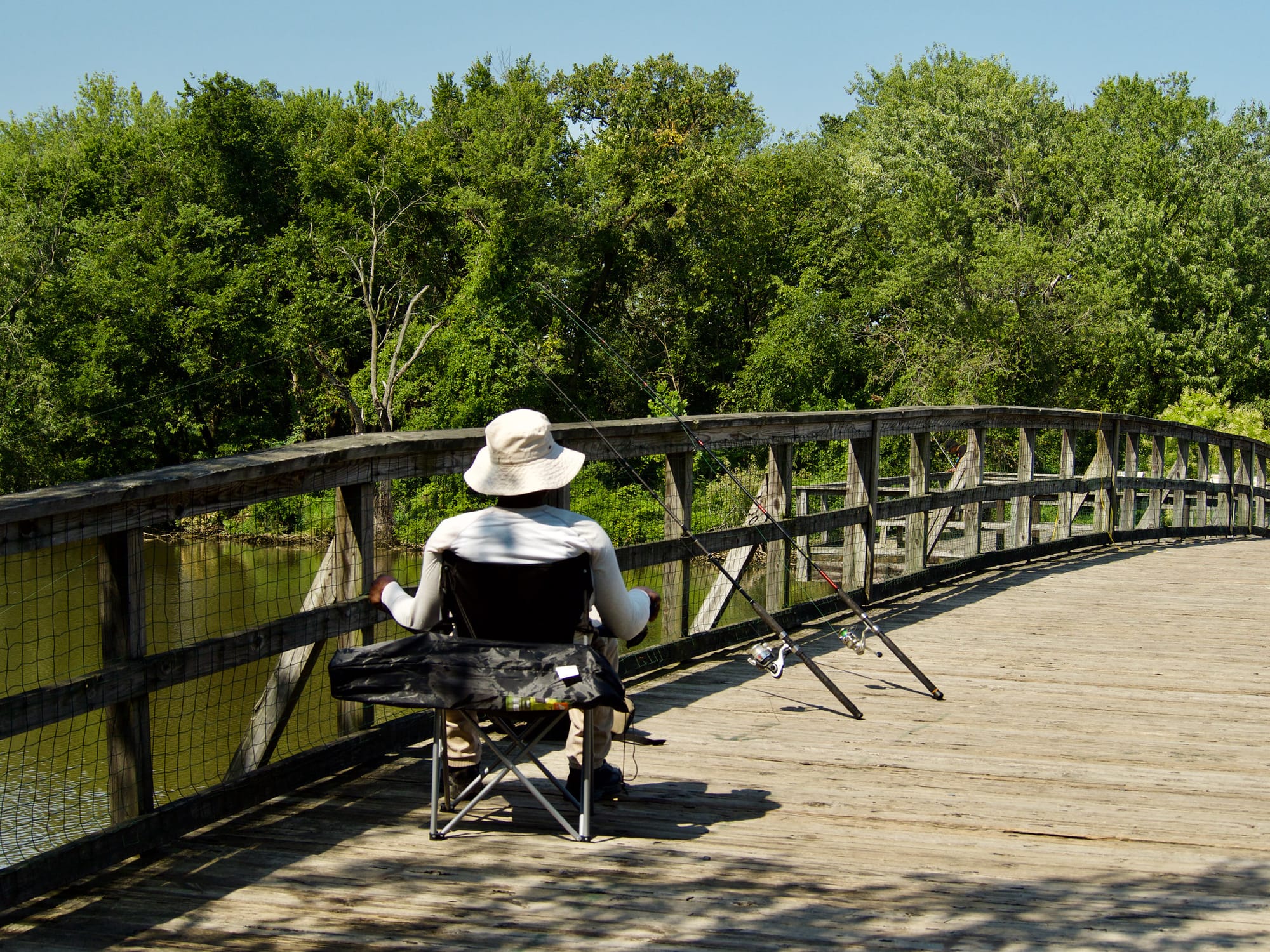 A person sitting on a bridge next to fishing poles