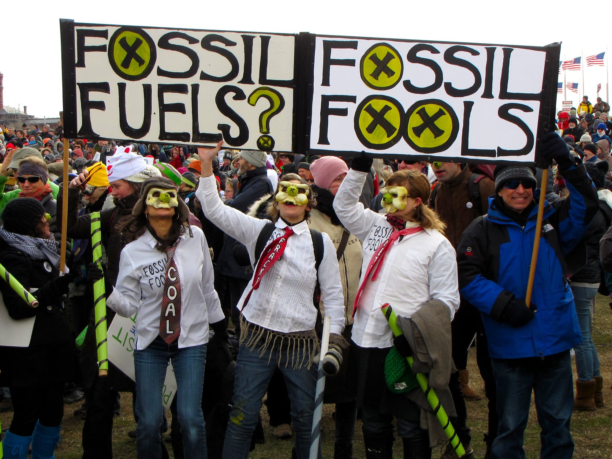 People in masks holding a sign that reads Fossil Fuels? Fossil Fools 