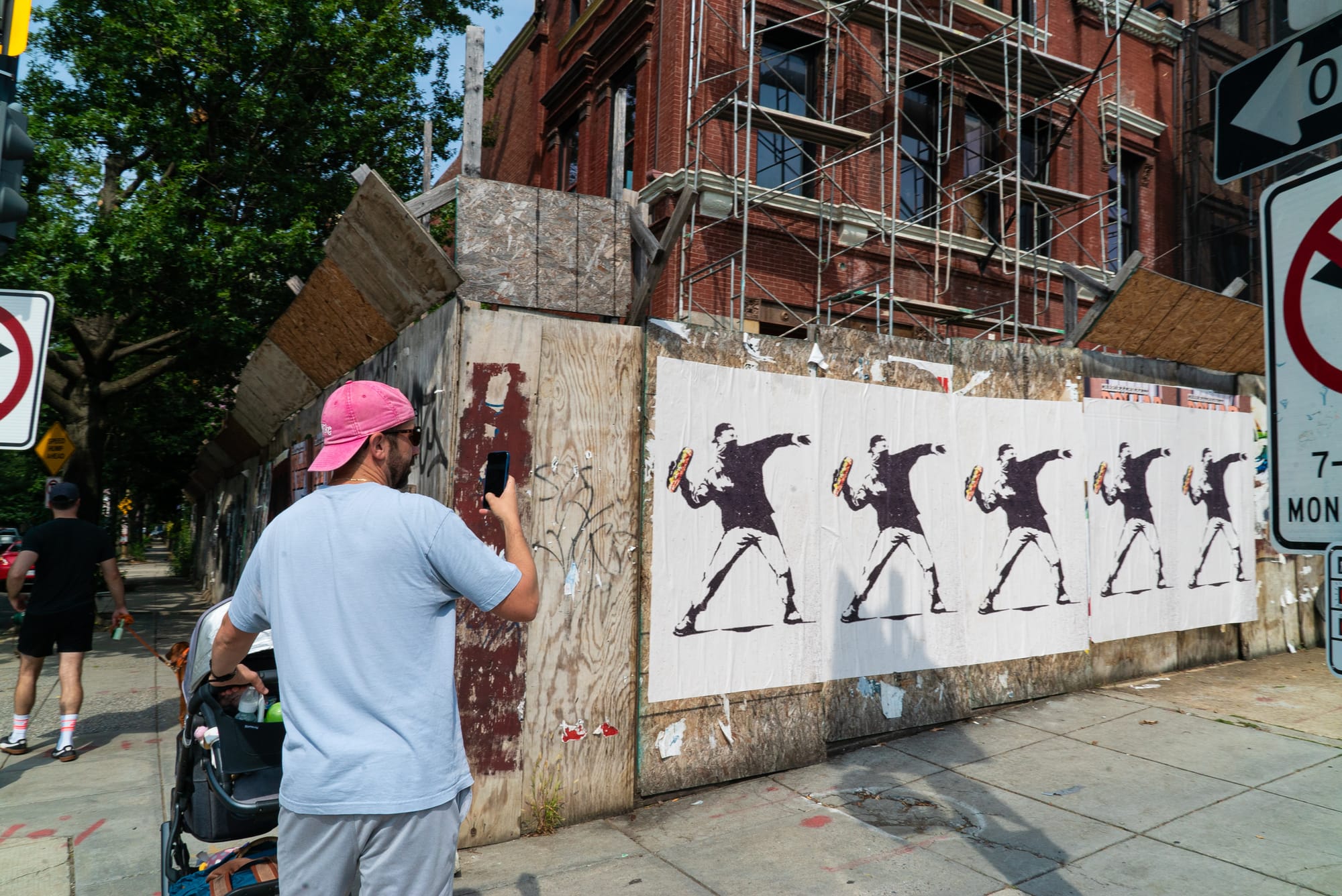 A man photographs a series of posters showing a man throwing a sub in the style of Banksy.