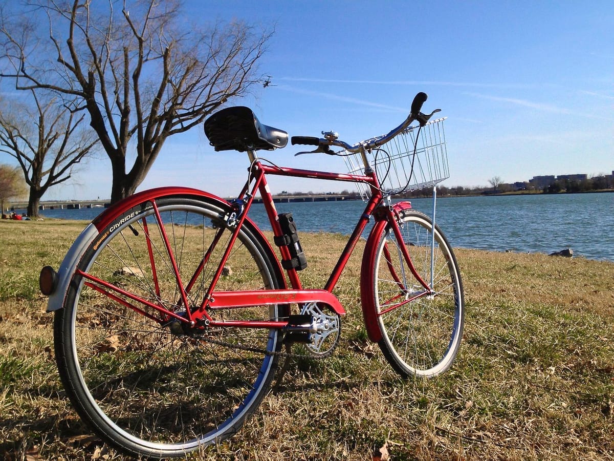 A red bike sits on grass near waterfront.