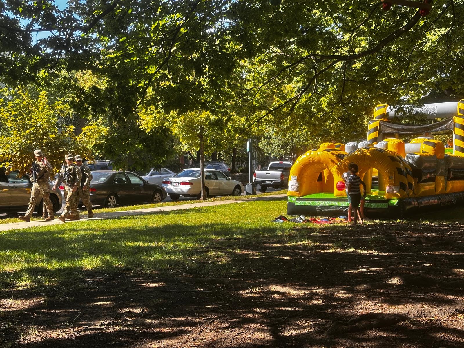 Photo showing three National Guard members armed with rifles walking down a D.C. sidewalk next to children playing.