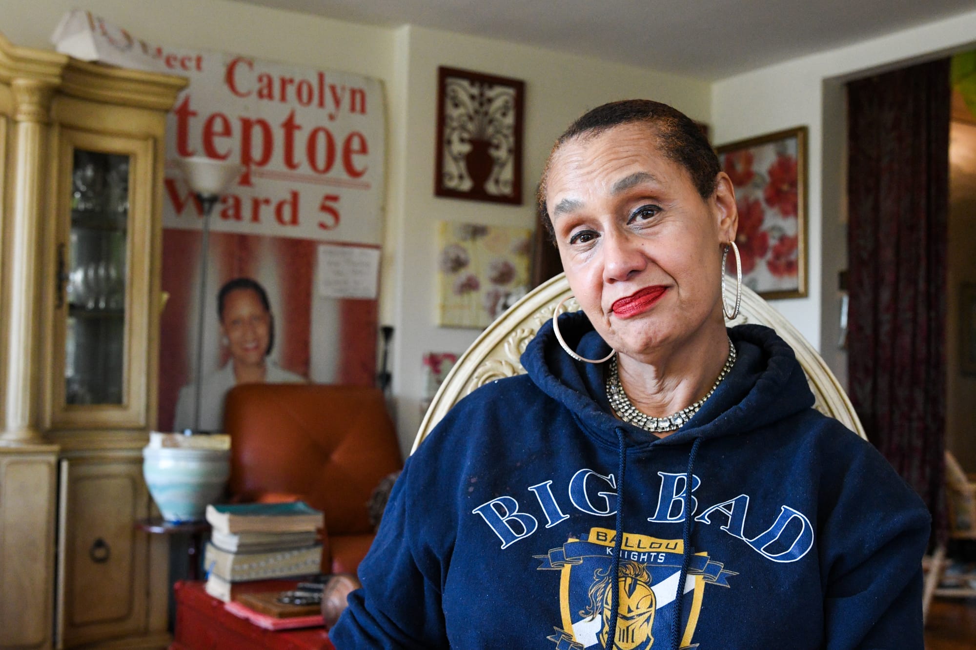 A woman in a blue "Big Bad Ballou Knights" sweatshirt — from Balout Senior High School, a D.C. public school — in her living room.