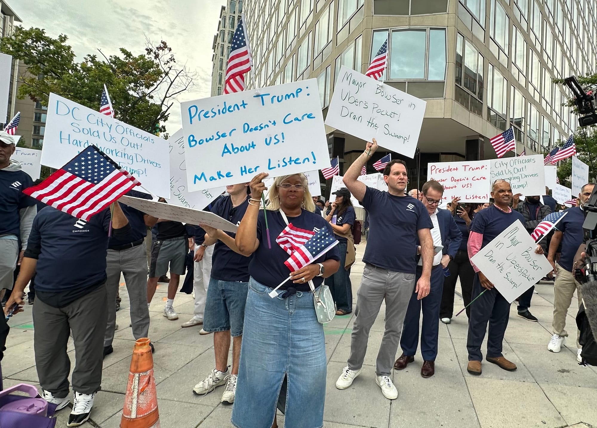 A group of people holding American flags and handwritten protest signs with messages to President Trump.