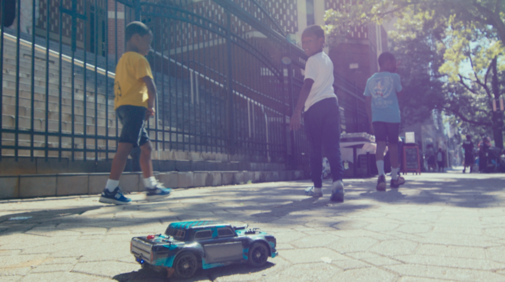 Three kids playing on a street look back at a toy car.