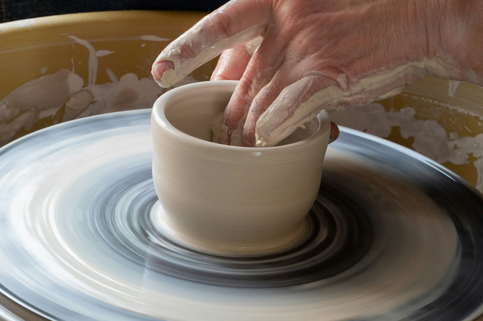 A mid-process shot of someone throwing a pot or cup on a pottery wheel.