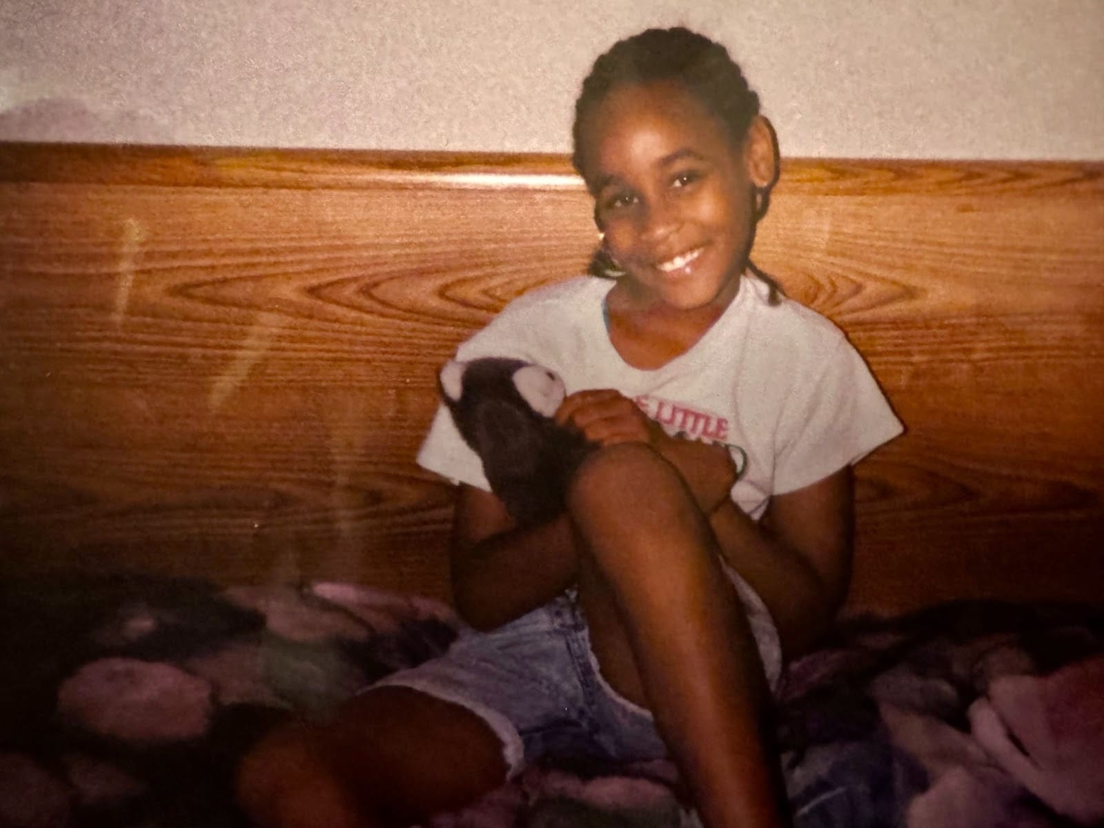A young girl, smiling and sitting holding a stuffed animal.
