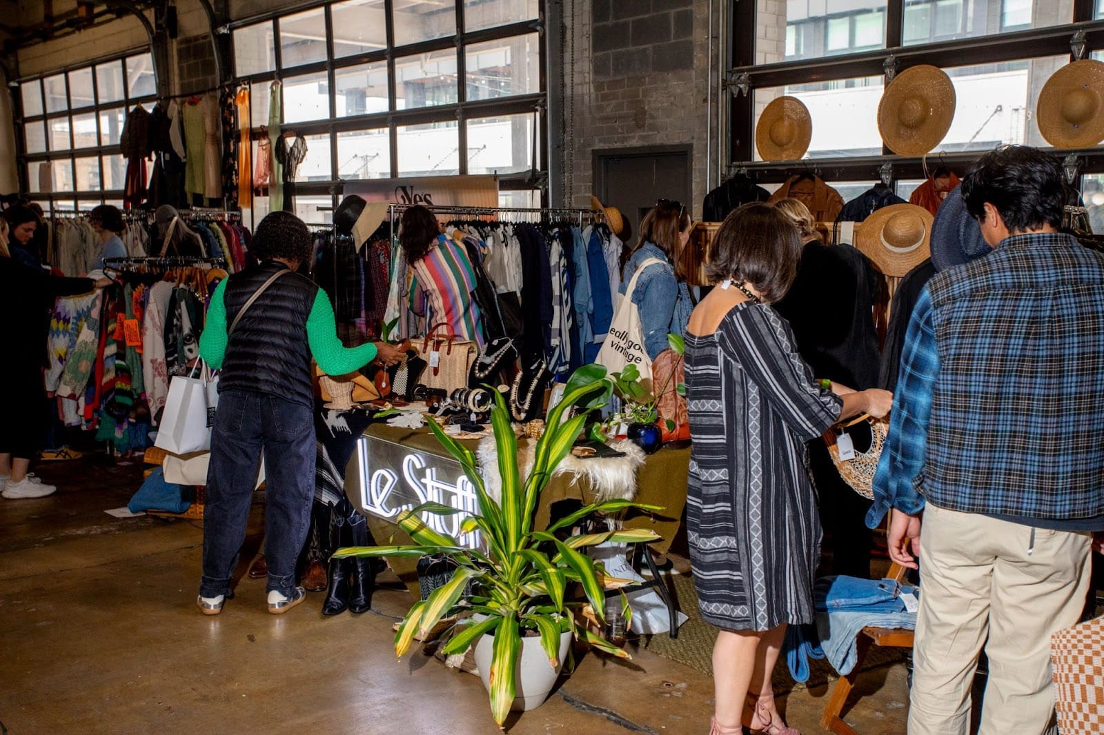 Shoppers browse vintage clothing and accessories in a warehouse space.