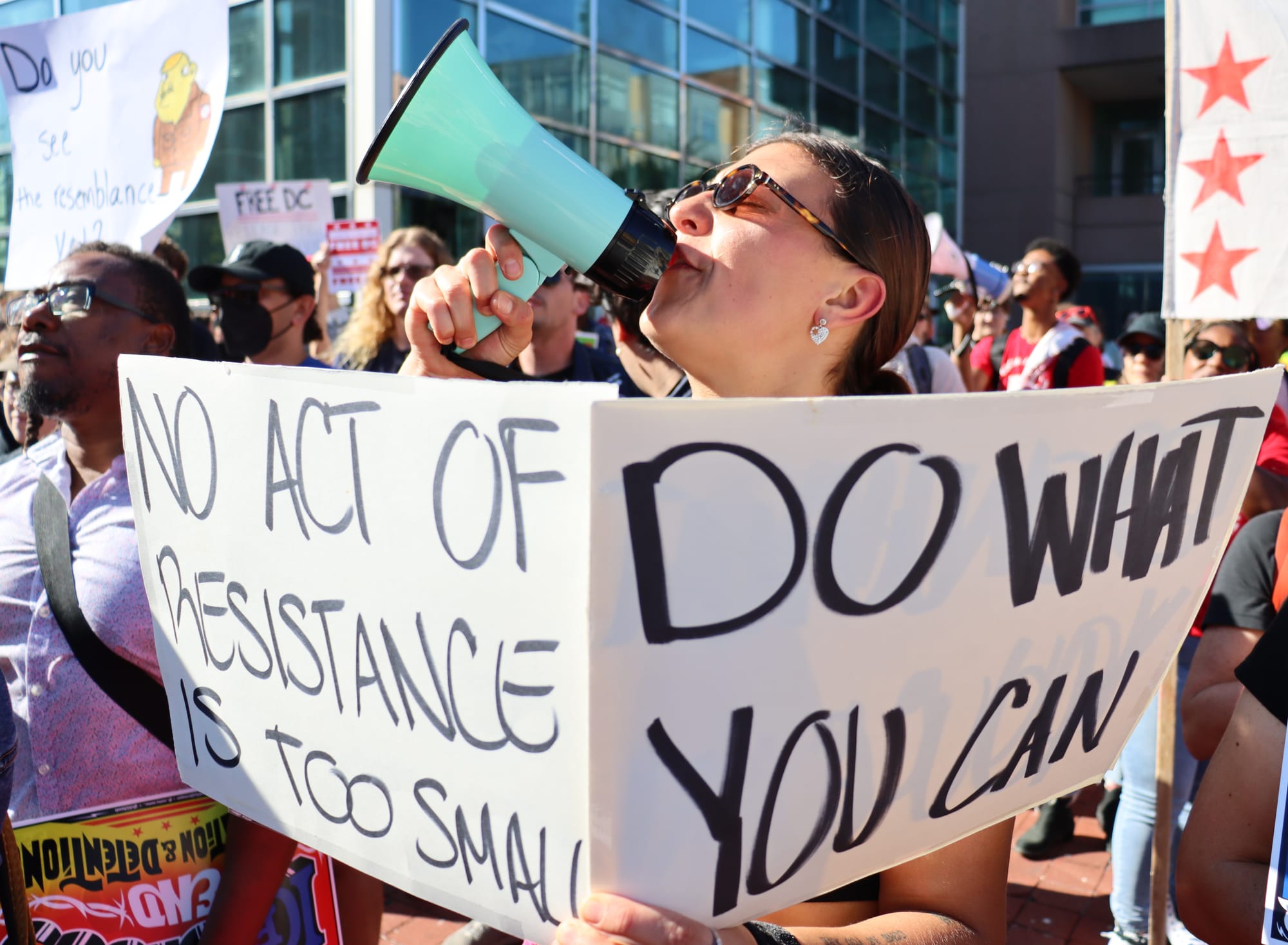 Someone speaks into a bullhorn at a rally holding a sign that says: "No act of resistance is too small" and "Do what you can."