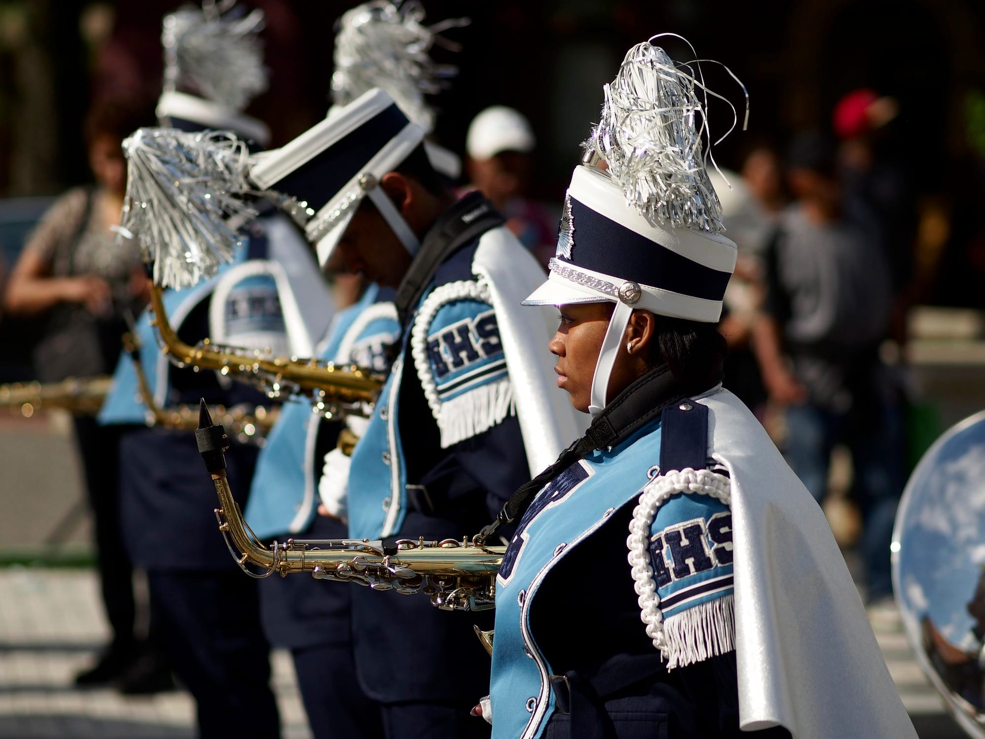 Members of a high school marching band wearing blue and white uniforms and holding saxophones