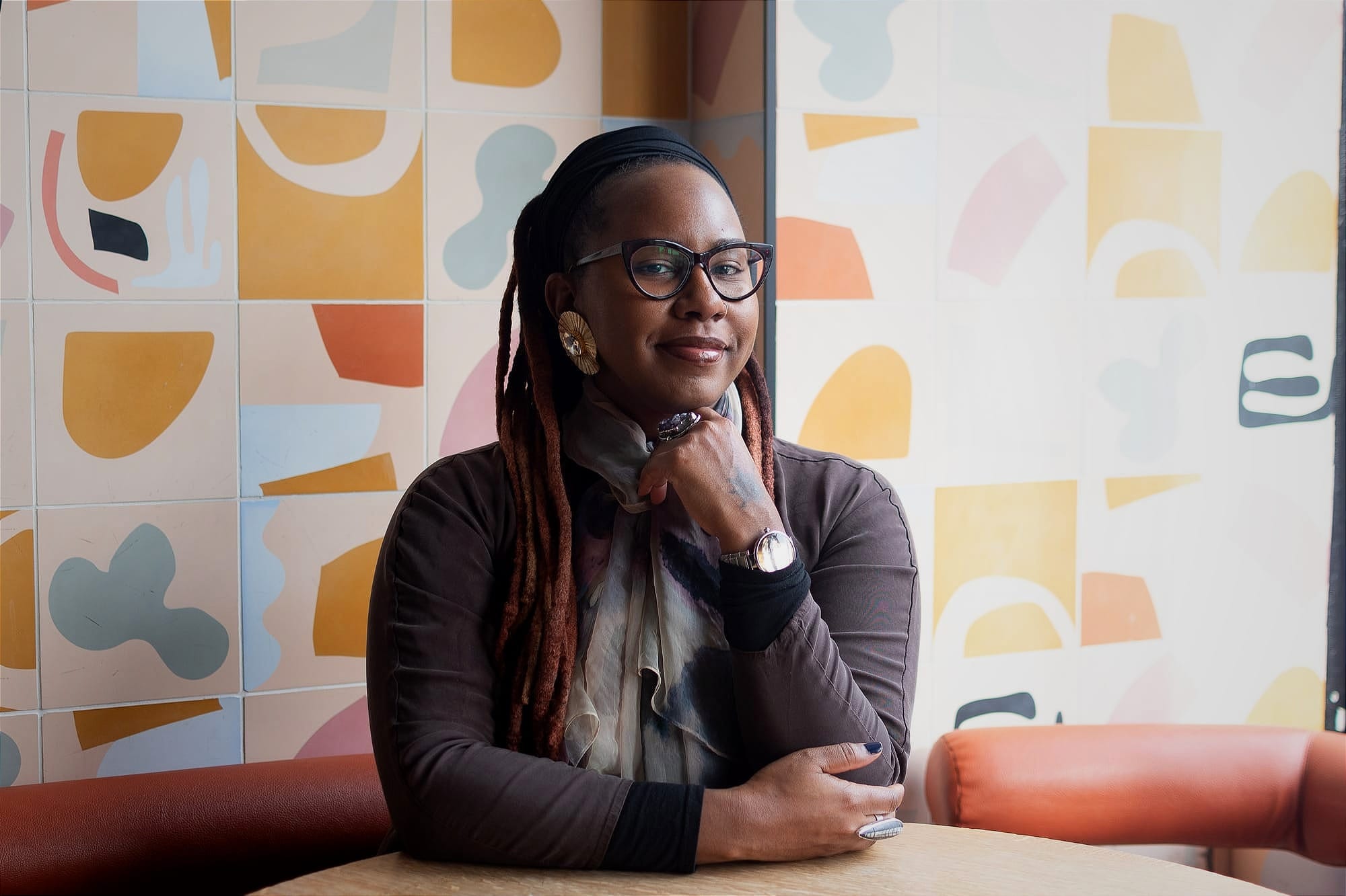 A photograph of a person with their hand under their chin with a colorful background