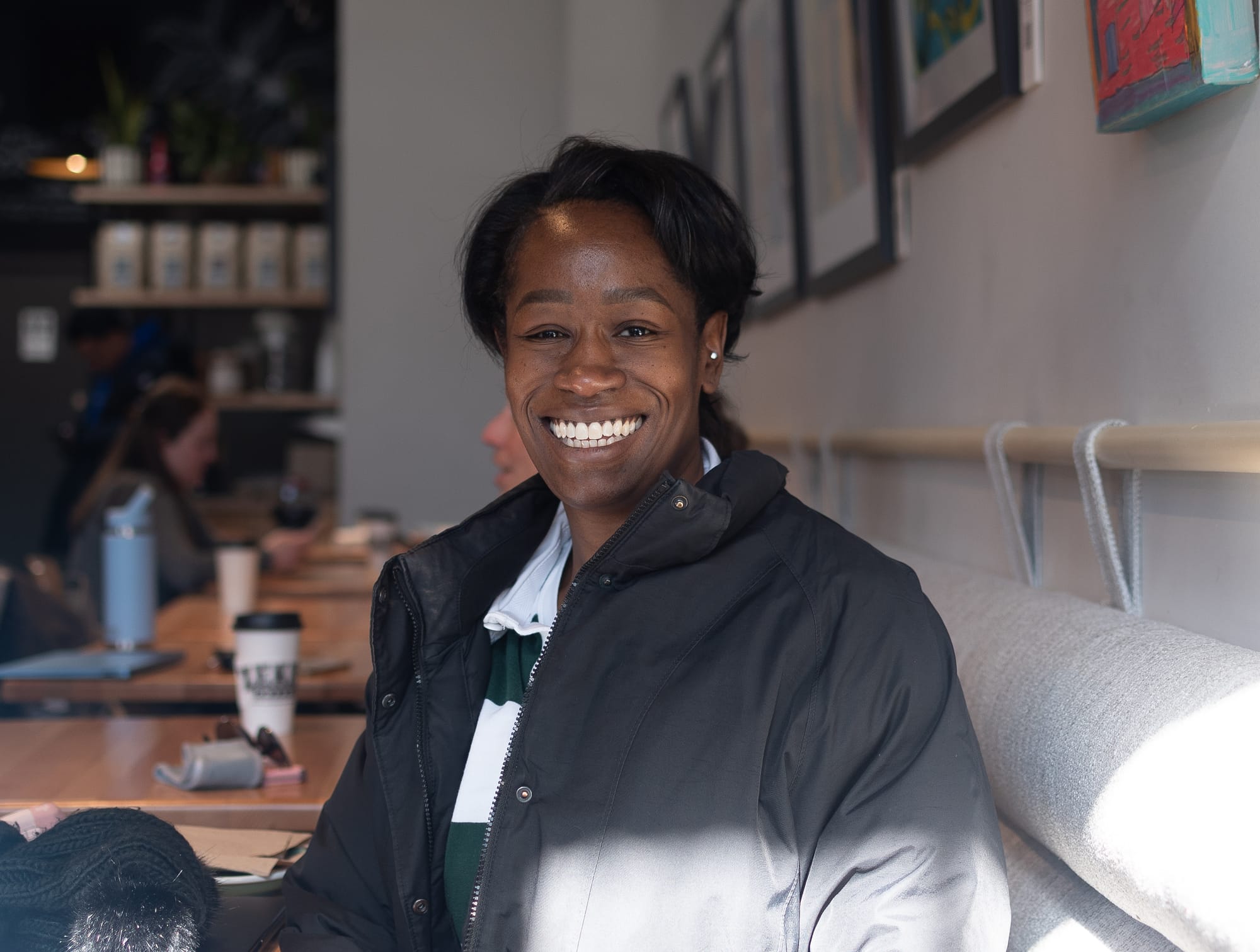 A photograph of a person smiling inside a coffee shop.