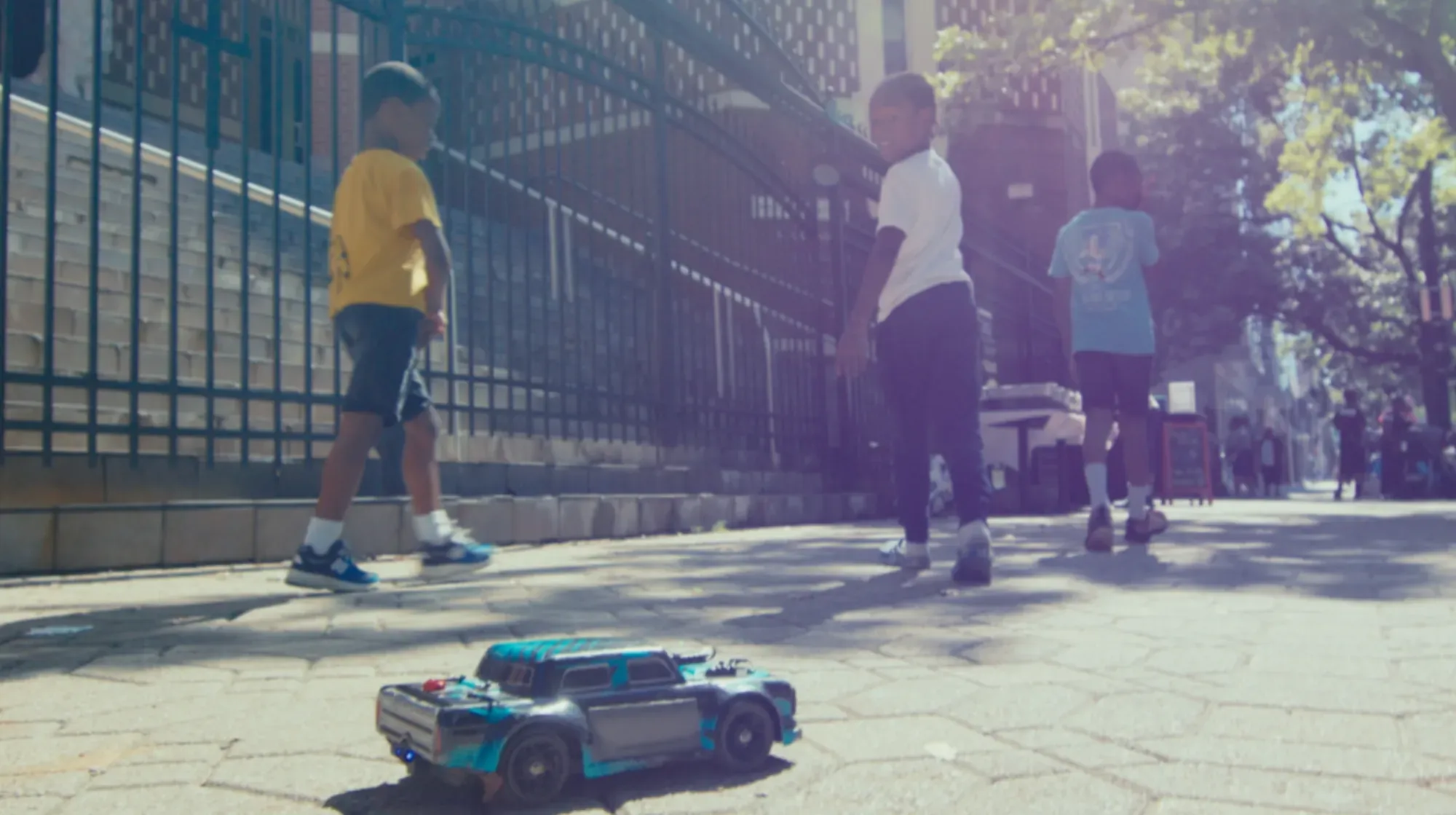 Three kids walk down a sidewalk with a toy car