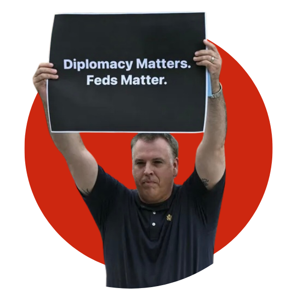A portrait of Michael Duffin agaisnt a red background, he's holding a sign that reads "Diplomacy Matters. Feds Matter."