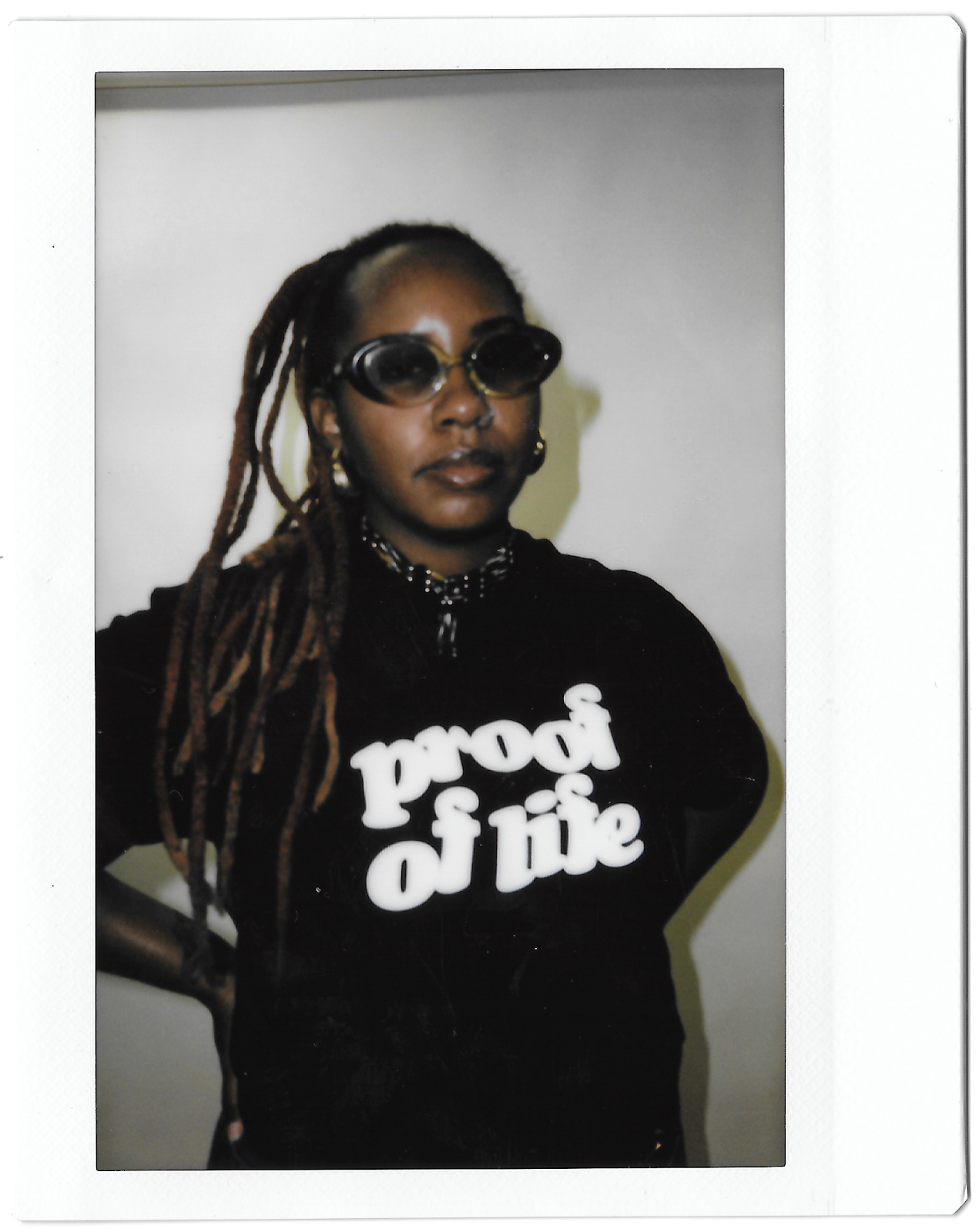 A Polaroid portrait of Dee Dwyer wearing a shirt that reads "Proof of Life."