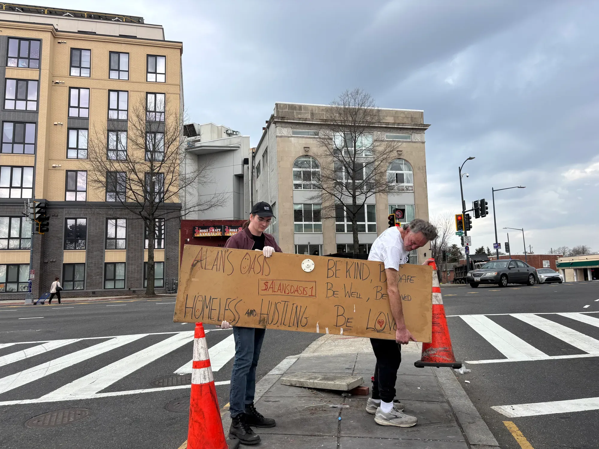 Alan and a friend carry his sign from the median where he hands out water.
