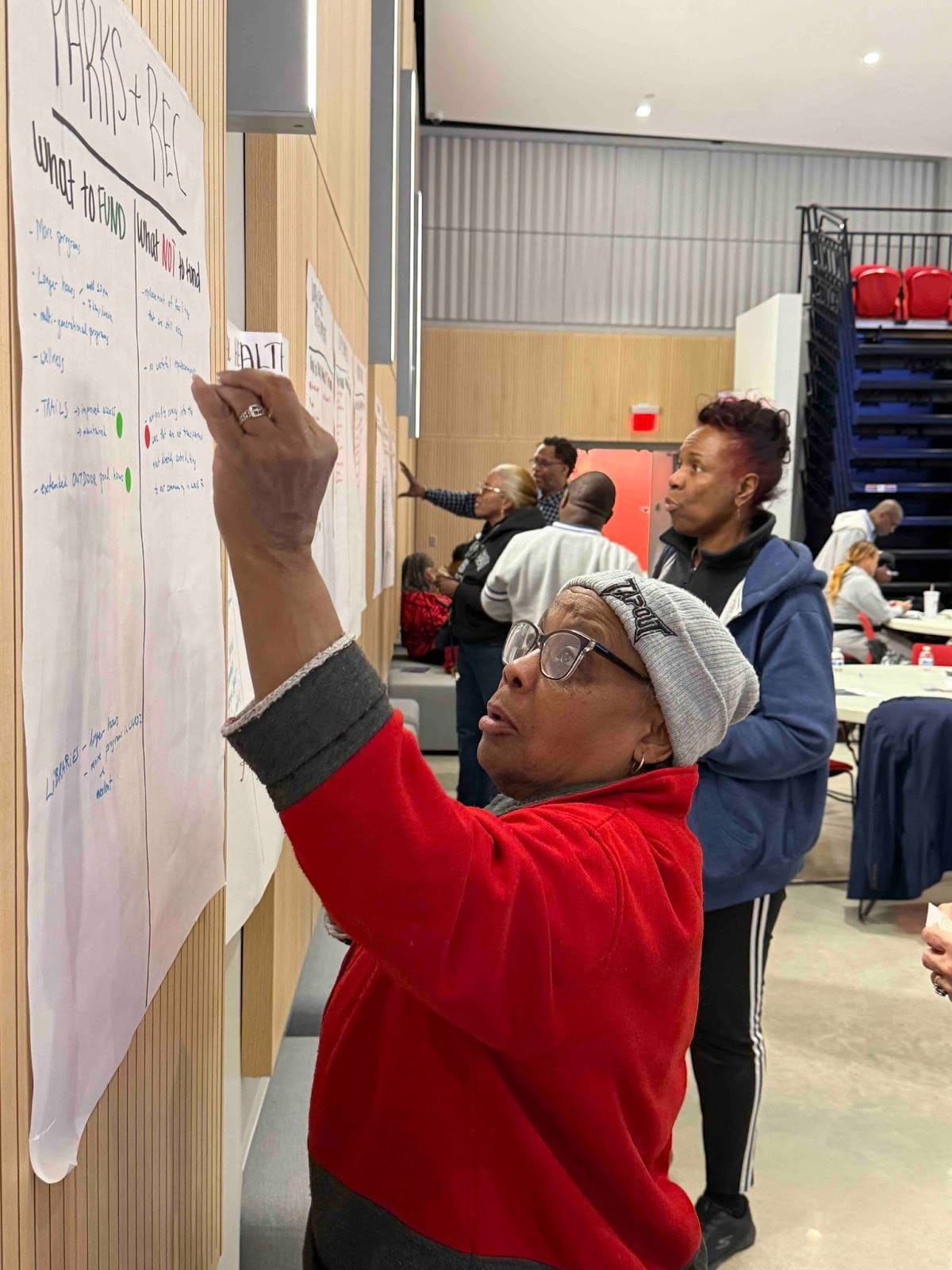 A person in a red jacket writes budget priorities on a large sheet of paper.