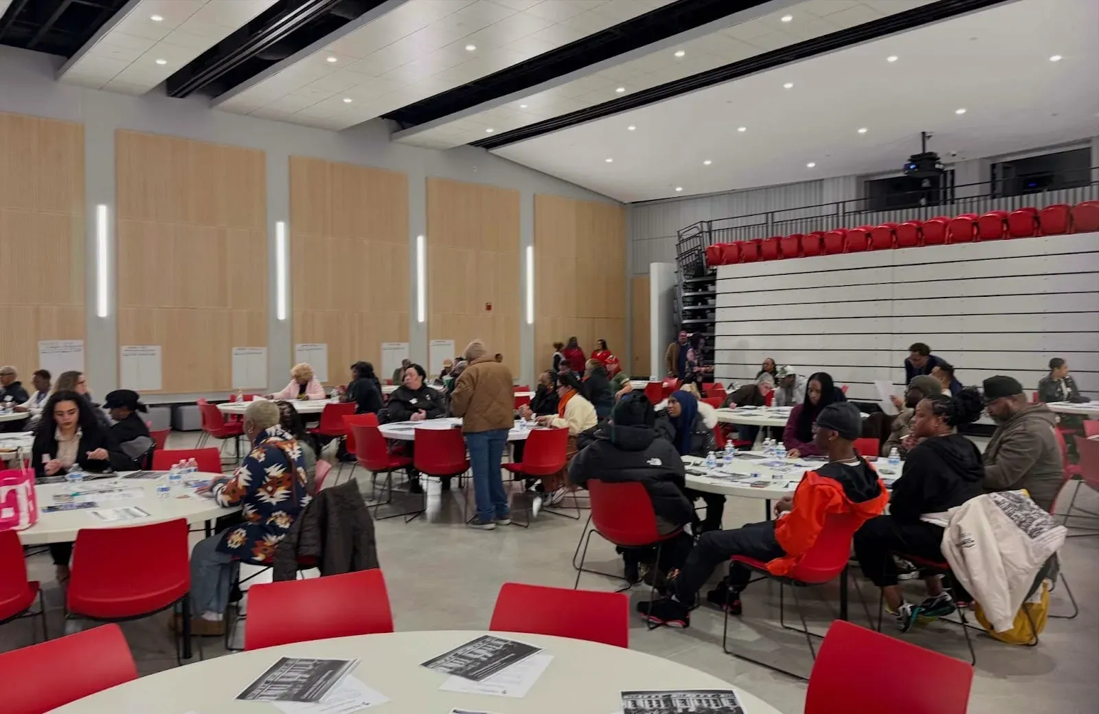 Residents gather around cafeteria tables in red chairs to rank their budget priorities.