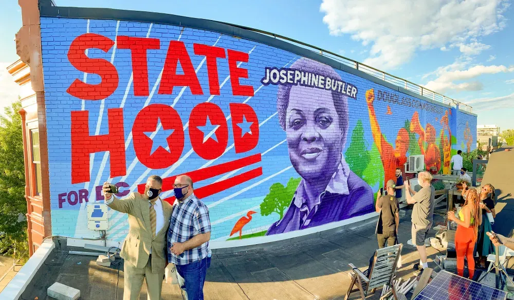 Mural that says statehood in red letters with people taking a photos of it.