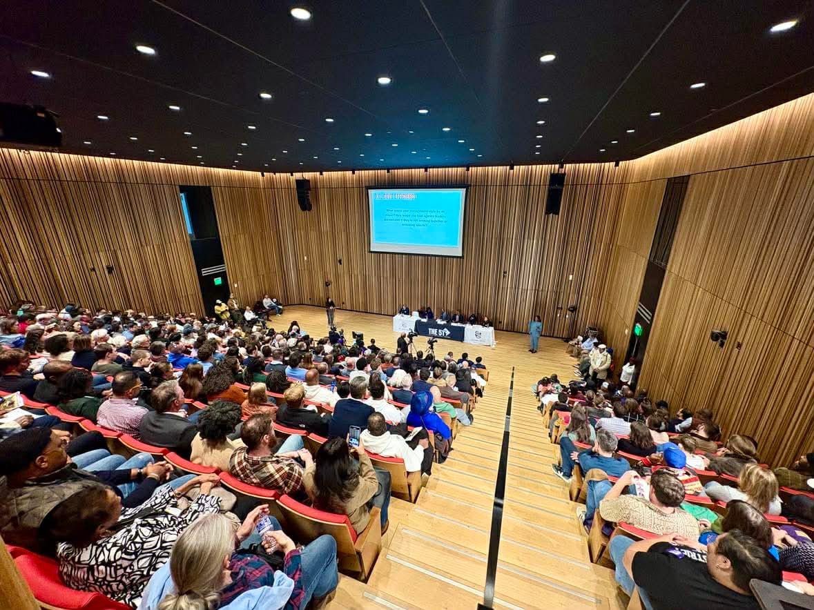 Over 300 people in seats at the Martin Luther King Memorial Library, with a large screen with the questions on it.