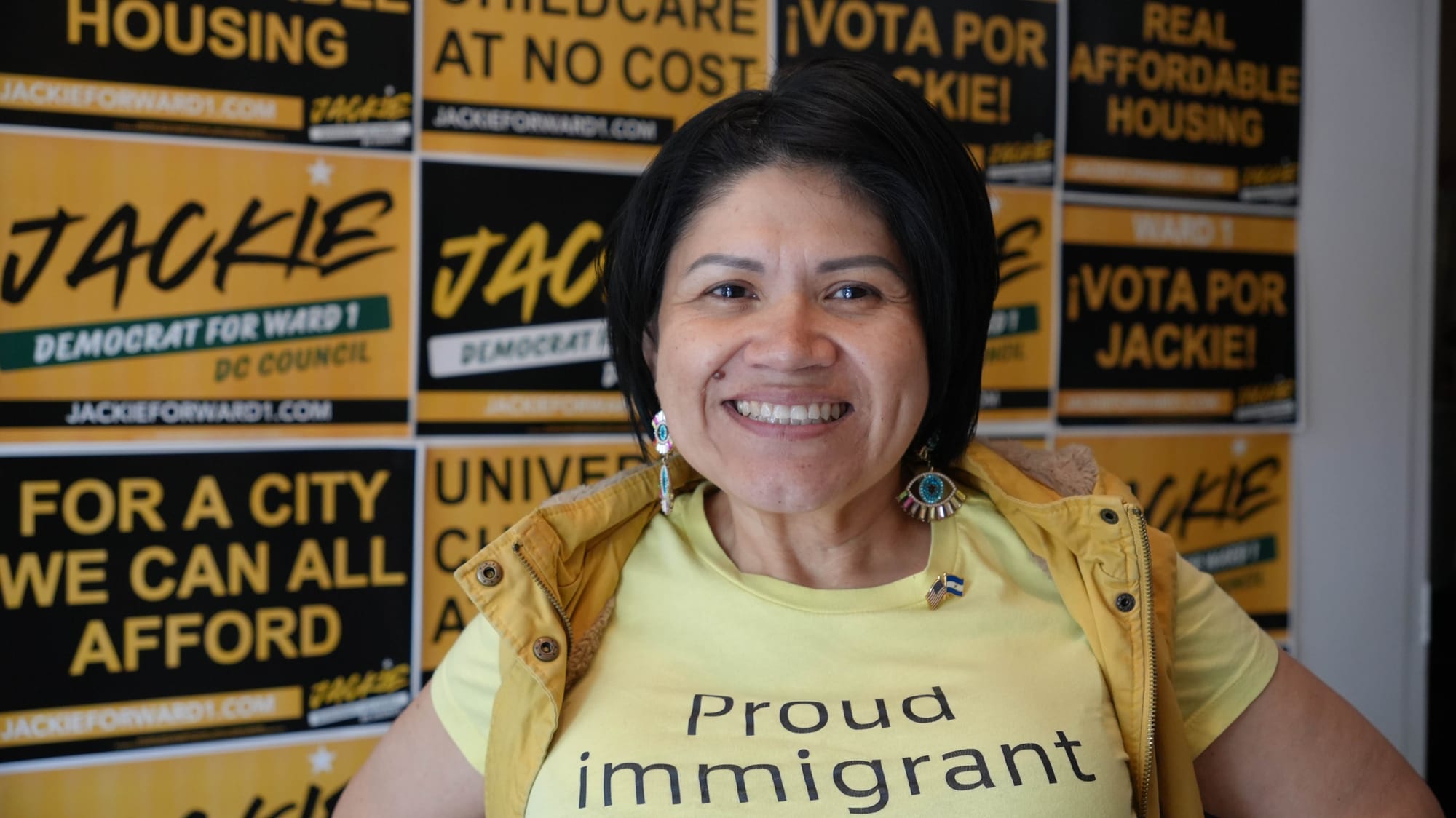 A photo of Jackie Reyes Yanes posing in her campaign office, with her yard signs in the background.