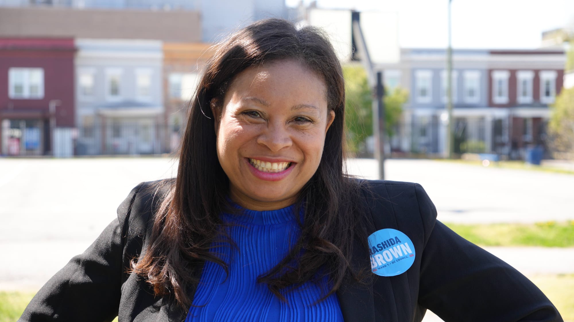 A photo of Rashida Brown posing and smiling as she stands in Bruce Monroe Park.