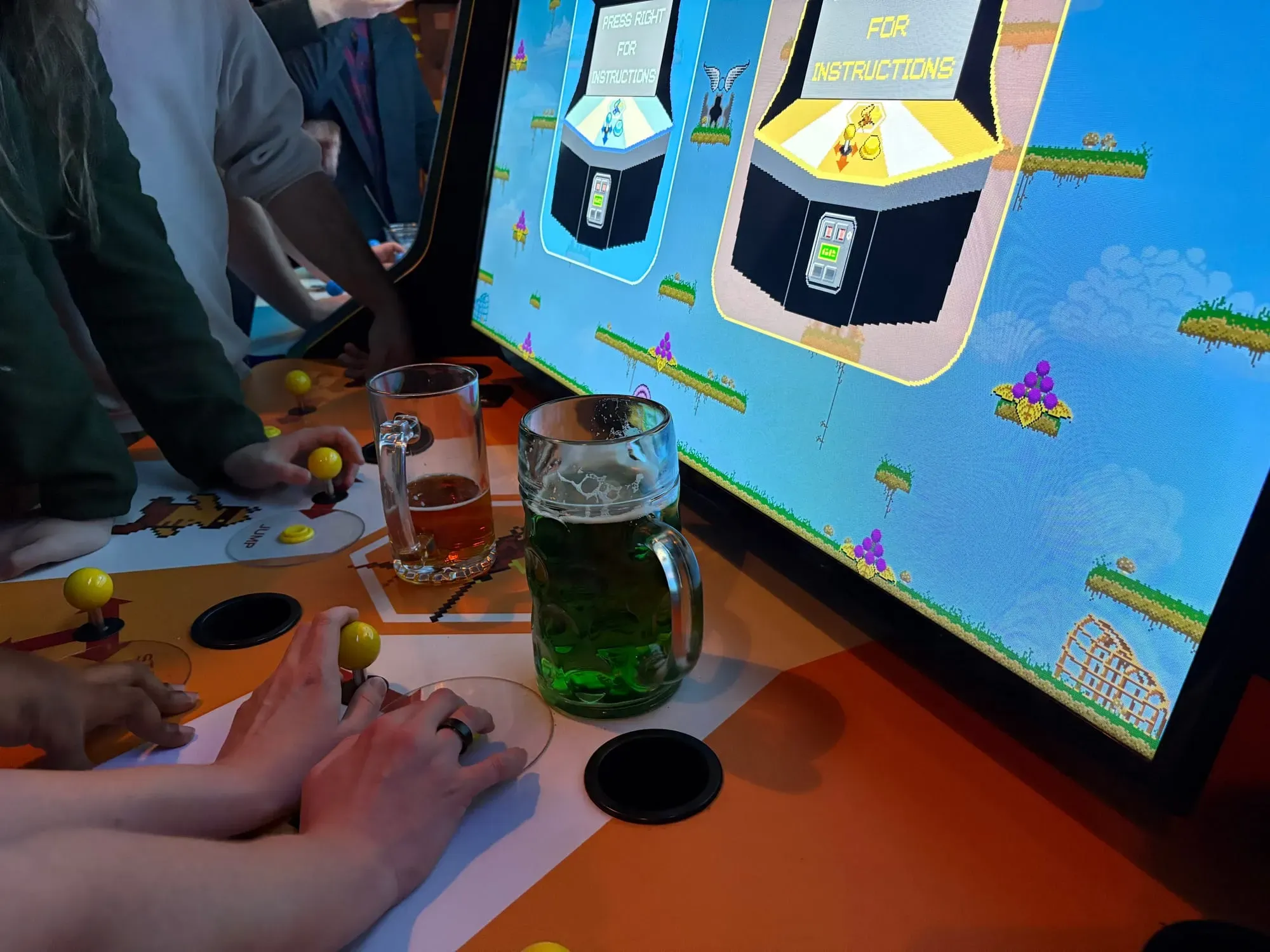 Two beers (one green) in front of the Killer Queen arcade game