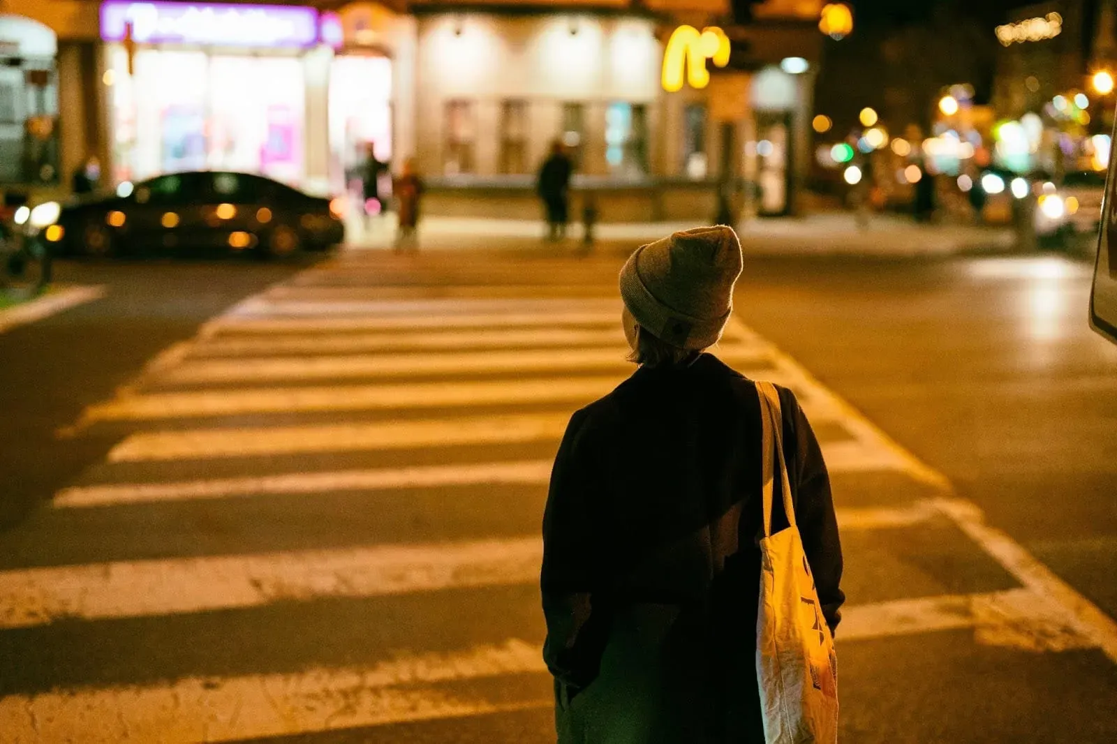 The back of a person with a tote bag about to cross the street in Adams Morgan.