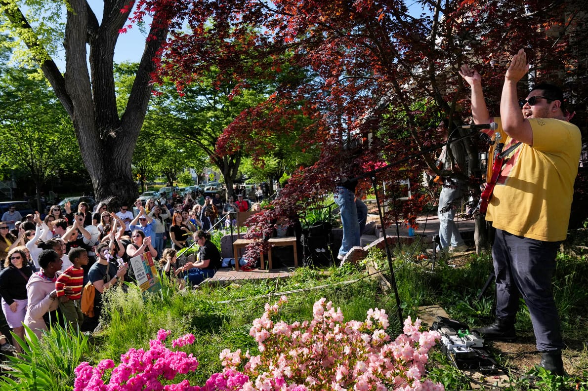 A band member leads an audience in clapping from a front yard in D.C.