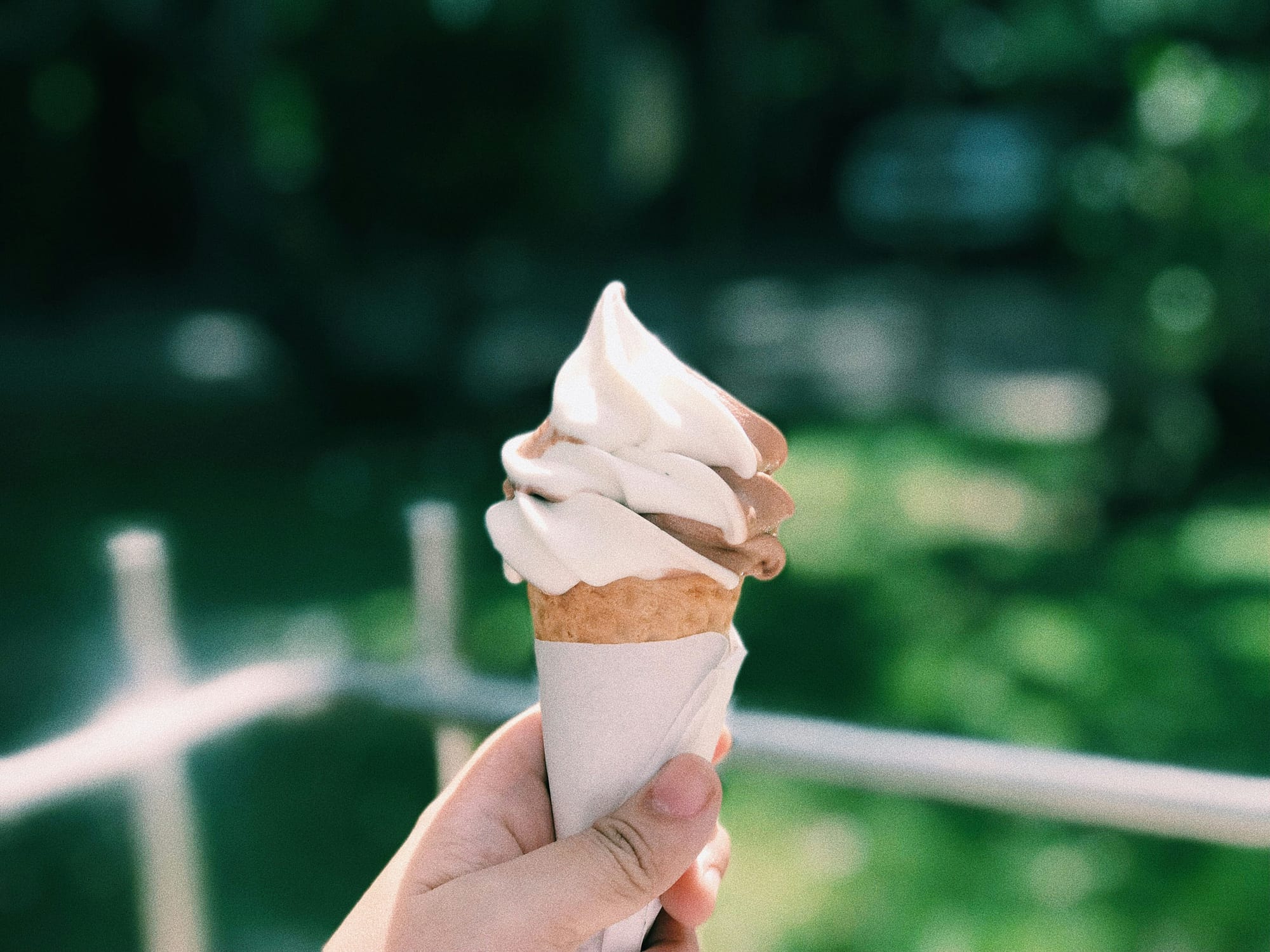 Someone holds a swirled soft serve cone outdoors.