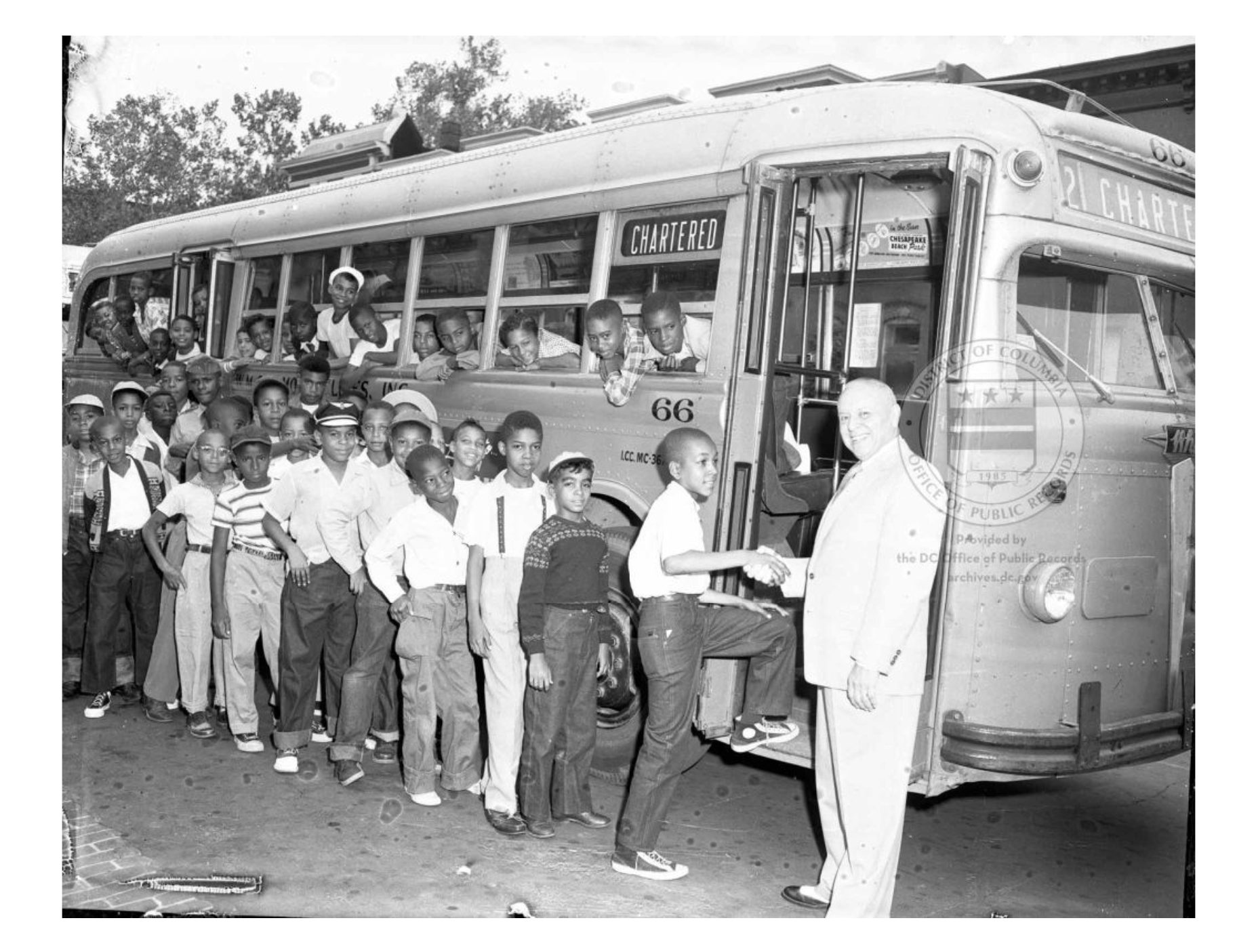 A line of Black children boarding a bus, while others lean out of the window. One is shaking hands with the DC comissiner