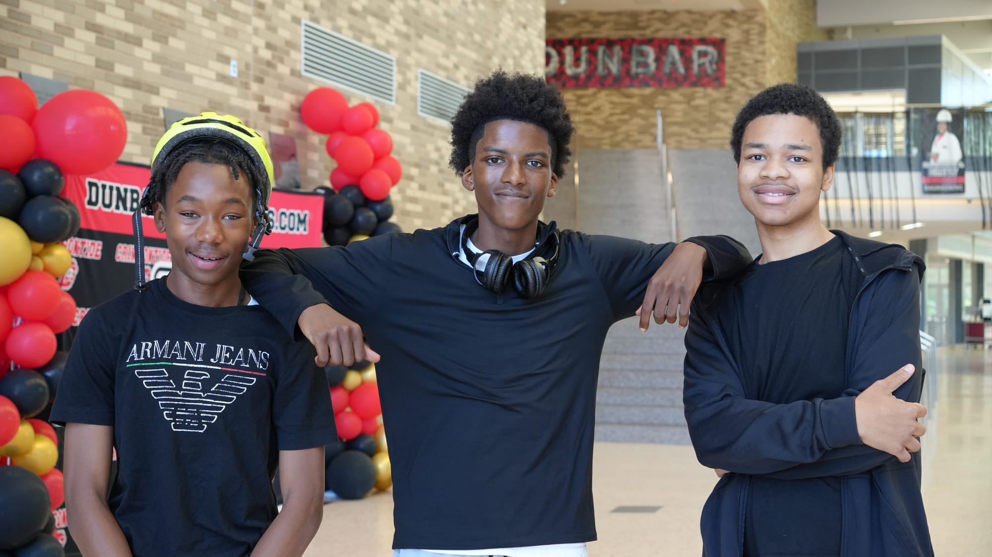A photo showing three students smiling together inside Dunbar High School. Parker is leaning his arms on the shoulders of Hailstorks and Gottschalk.
