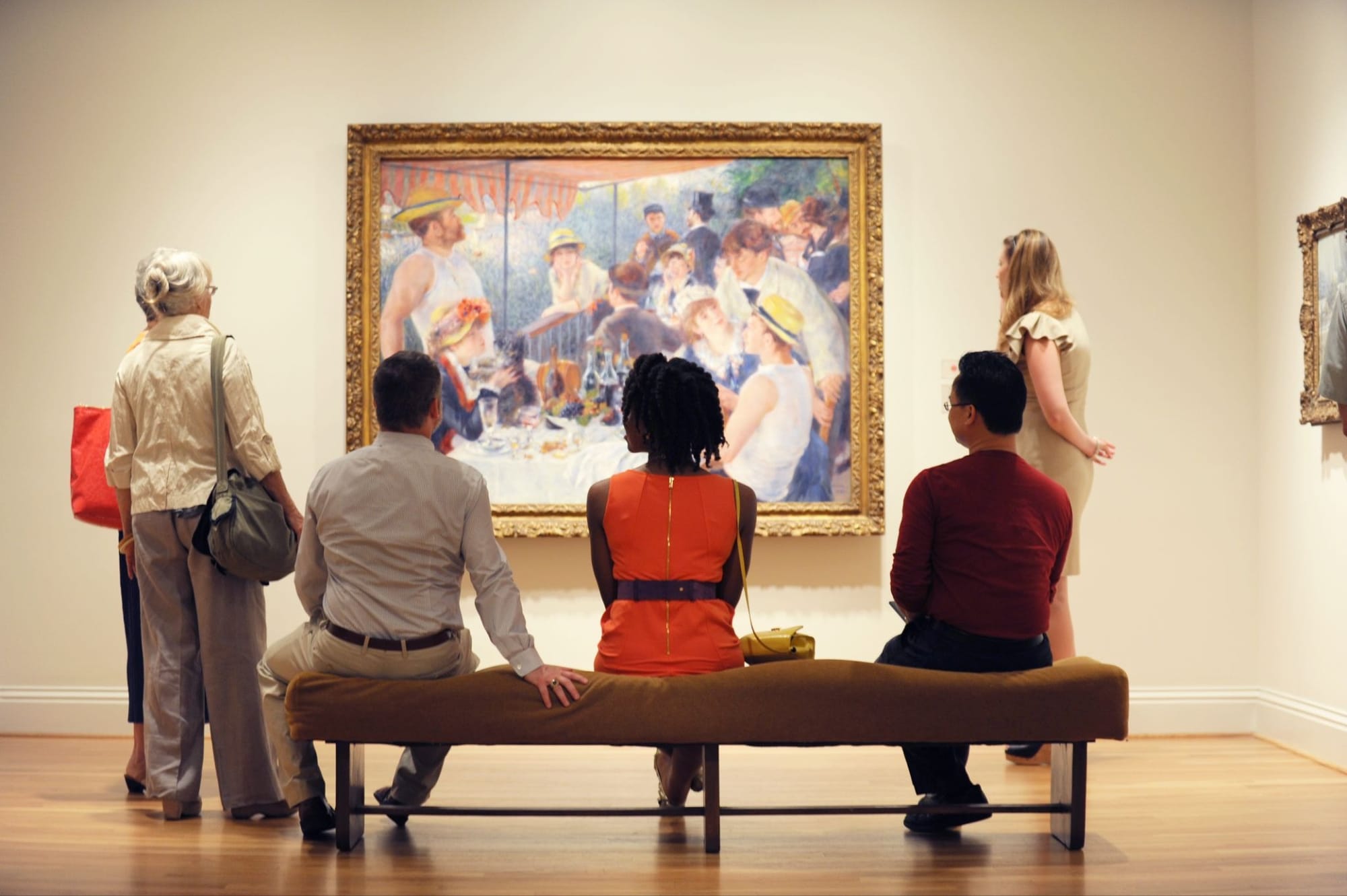 Three people sit on a bench looking at art.