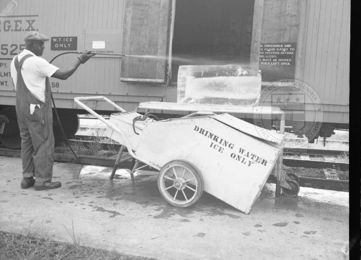 Photo showing a Black worker spraying a block of ice next to a cart that says "Drinking water ice only"