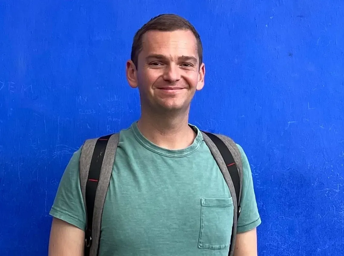 A portrait of Alex Koma in front of a blue wall