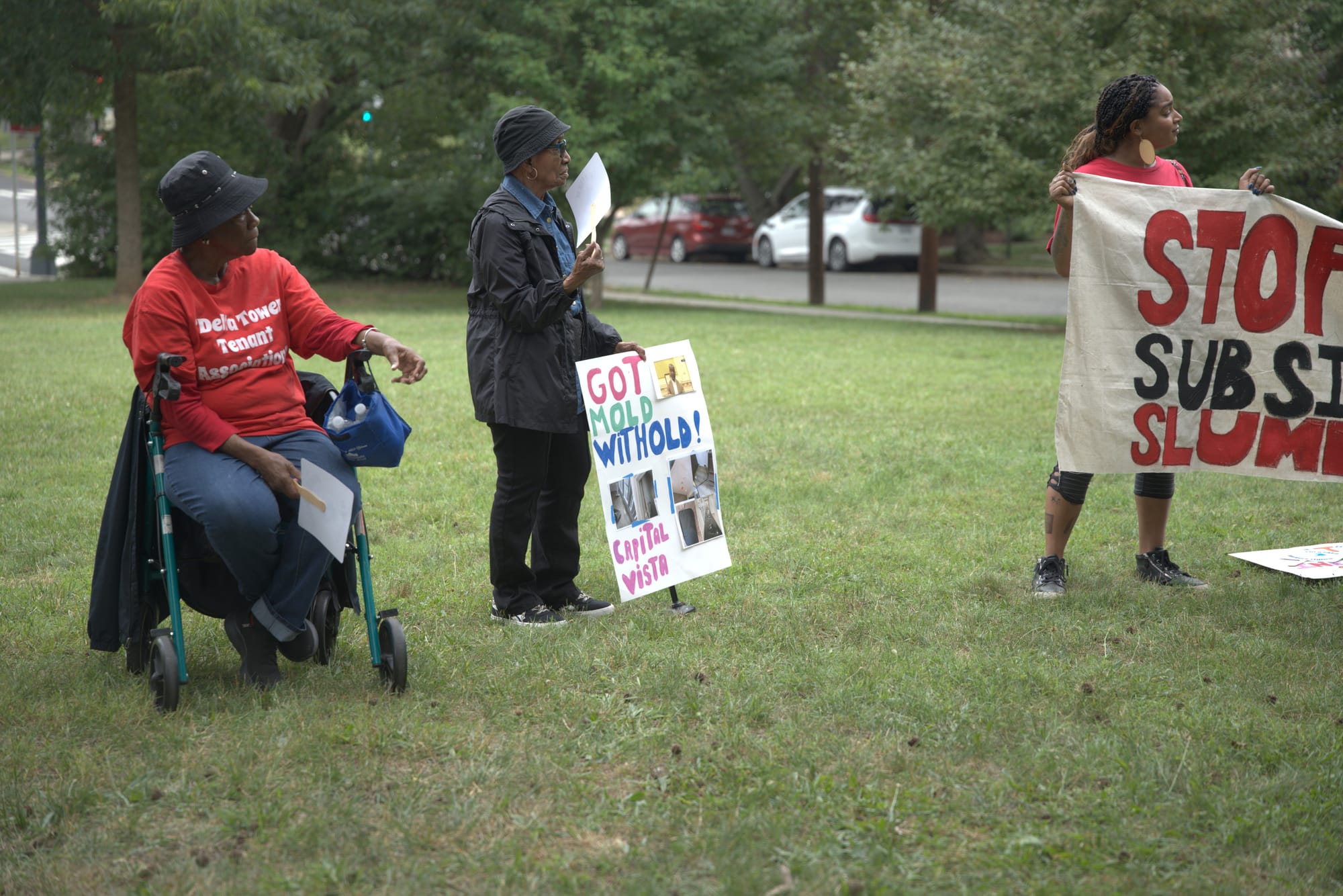 Three tenants in a park, one holding a sign that reads: "Got mold, withold!"