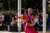Woman in red attire balances five hula hoops in an outdoor performance.