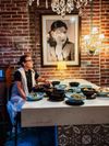 The owner of Nabiha, Nesrin Abaza, sits at a table covered in small plates of Palestinian food, with a black and white photograph of her mother behind her.