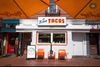 White brick exterior restaurant that reads La Tejana Tacos with orange chairs on a sidewalk.
