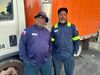 Photo of two men in city employee uniforms standing in front of a white and orange Department of Public Works truck